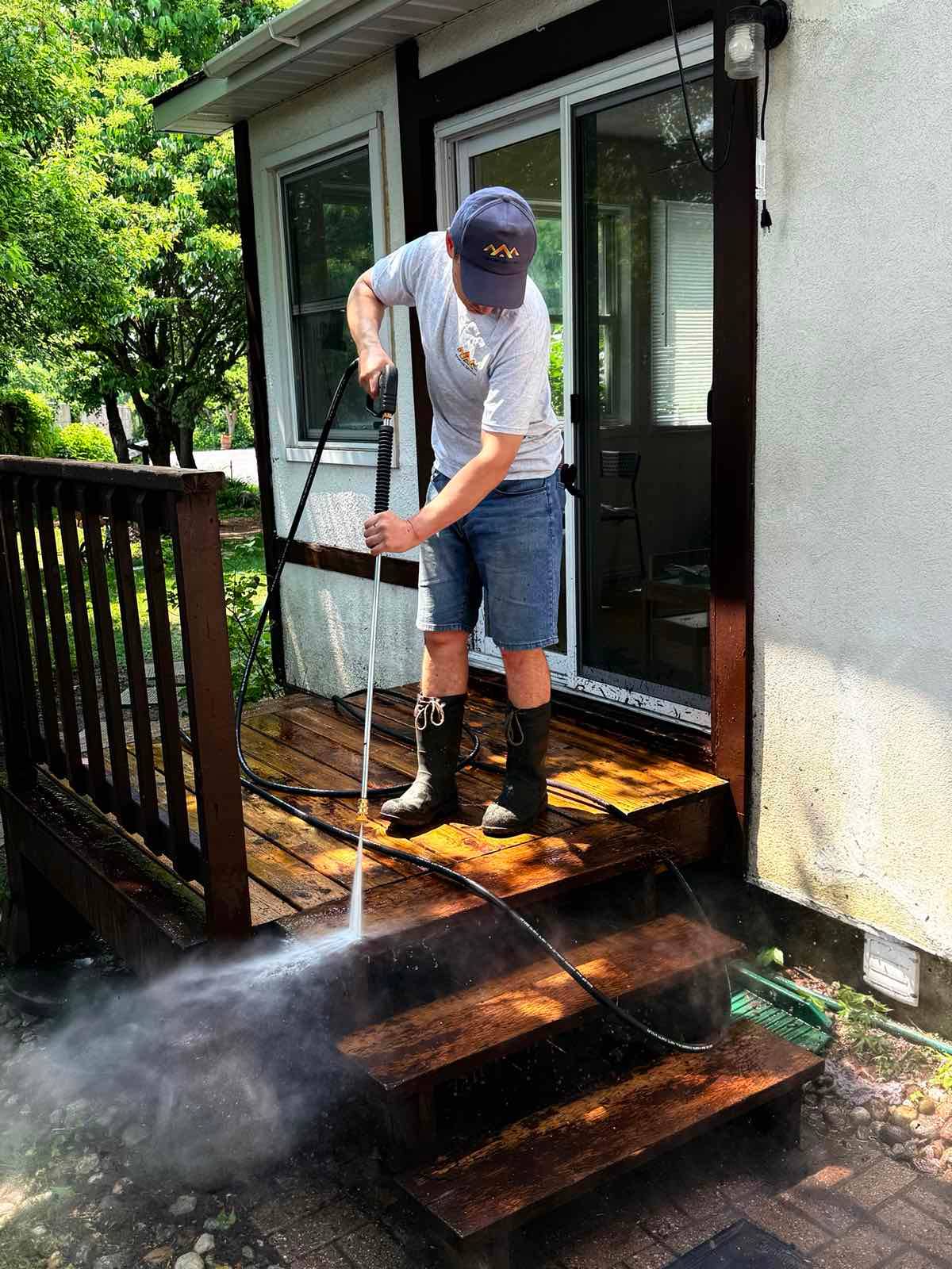Pressure washing a weathered wooden deck and stairs, spray lifting years of grime from the boards