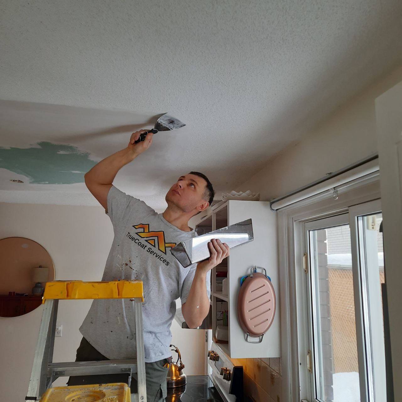 TrueCoat tradesperson skim-coating a repaired ceiling with a wide taping knife before repainting