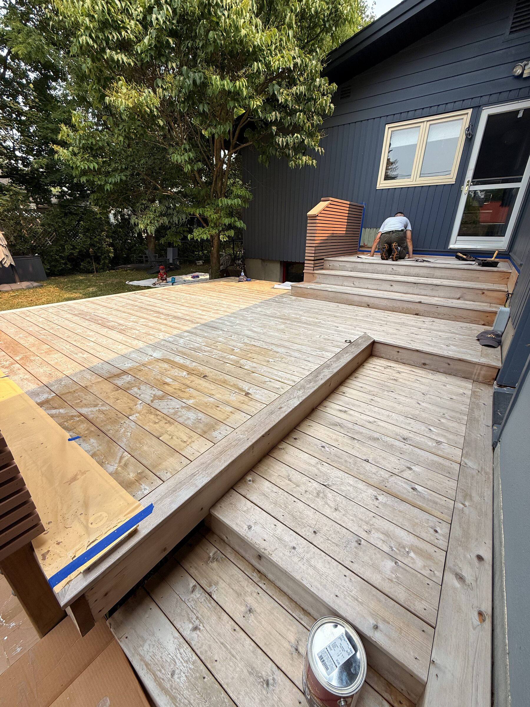 Before: Deck being stained by hand, painter's tape along the edge and a stain can in the foreground