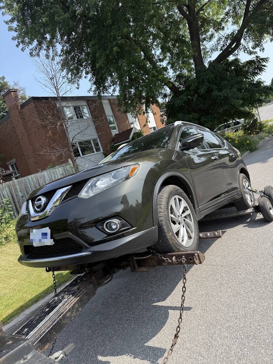 Dark grey Nissan SUV secured on a flatbed tow truck on a sunny residential street, Ontario license plate visible