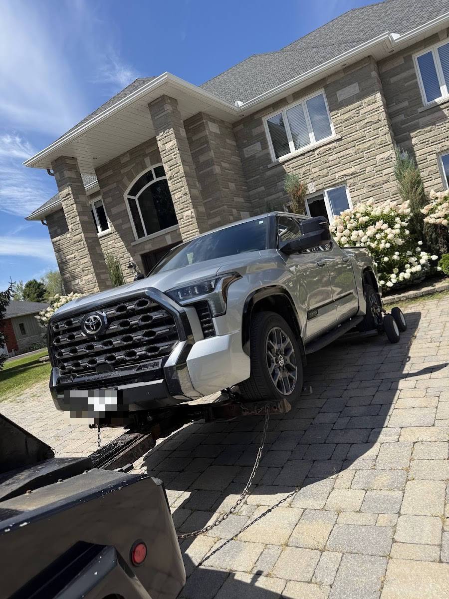 Grey Toyota Tundra pickup loaded on flatbed tow truck in driveway of large stone luxury home