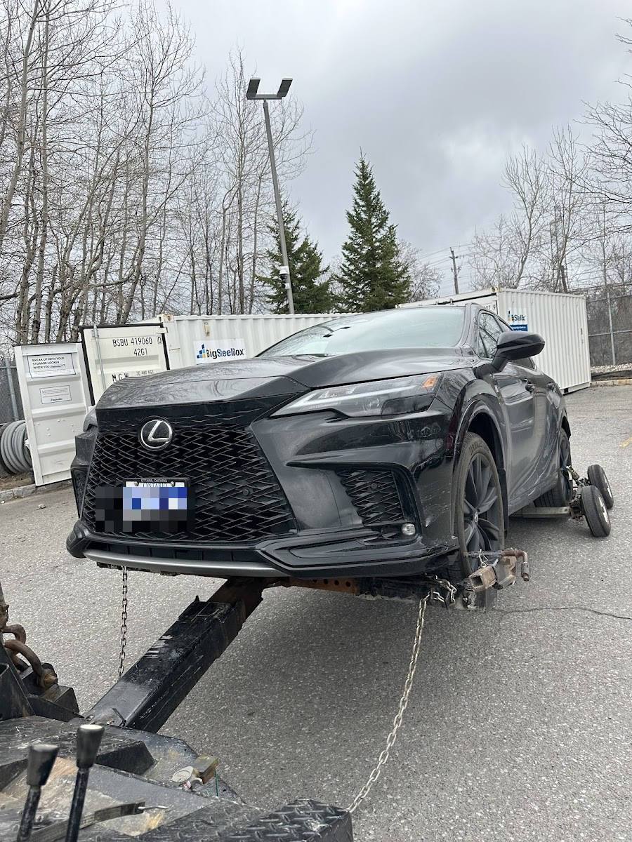 Black Lexus NX crossover with front fascia damage loaded on a tow dolly in a storage yard