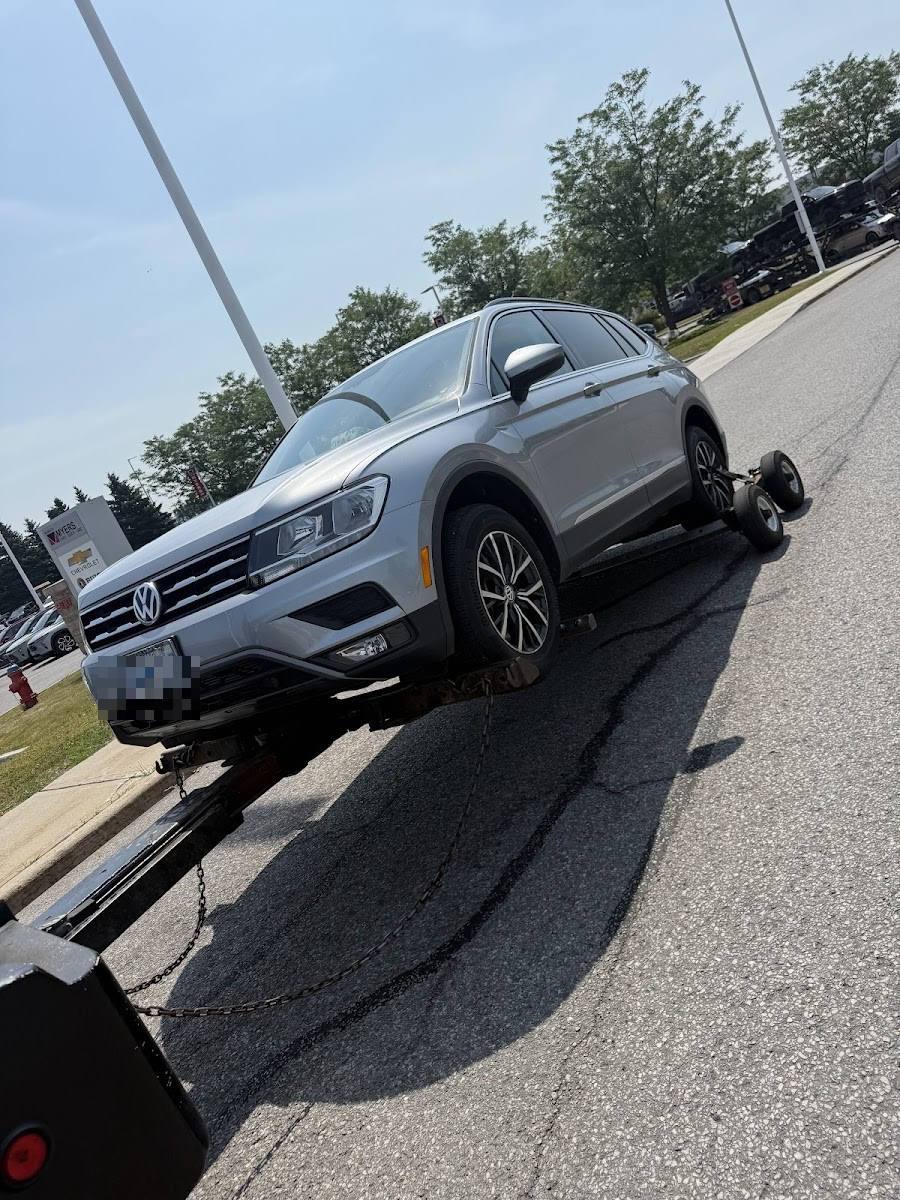 Silver Volkswagen Tiguan SUV secured on flatbed tow truck outside a Chevrolet dealership