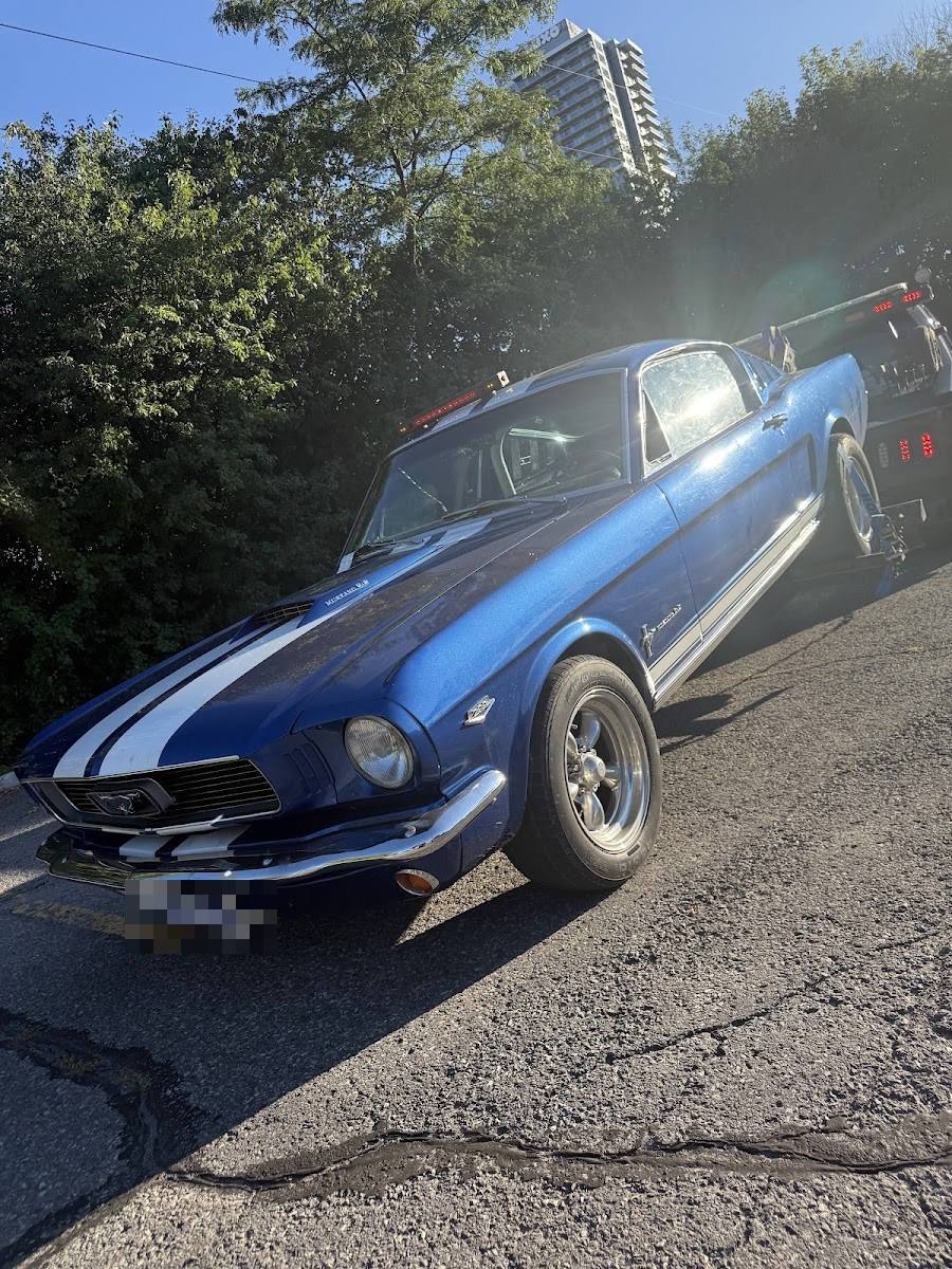 Classic blue Ford Mustang with white racing stripes being loaded onto a flatbed tow truck