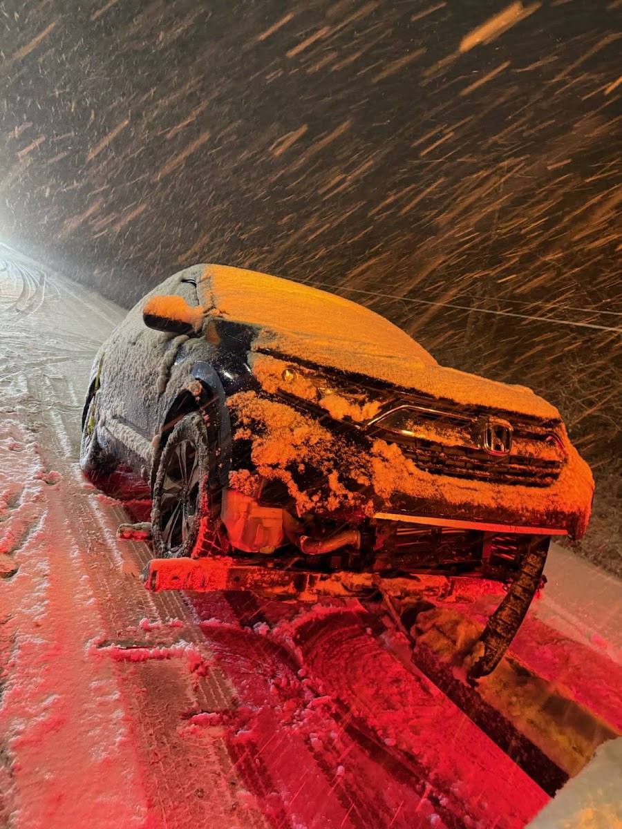 Snow-covered Honda CR-V SUV being recovered on a flatbed tow truck during a heavy nighttime blizzard